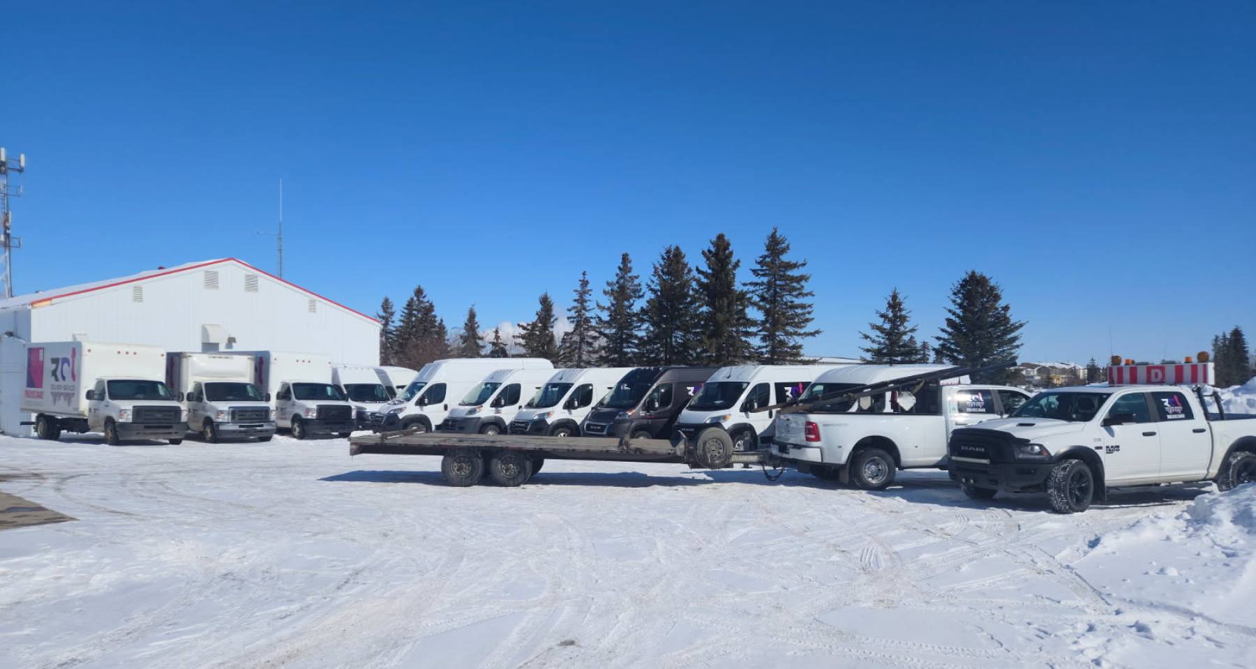 The RCT yard in winter: cube vans, cargo vans, a deck trailer, a one-ton dually and a pilot truck lined up.